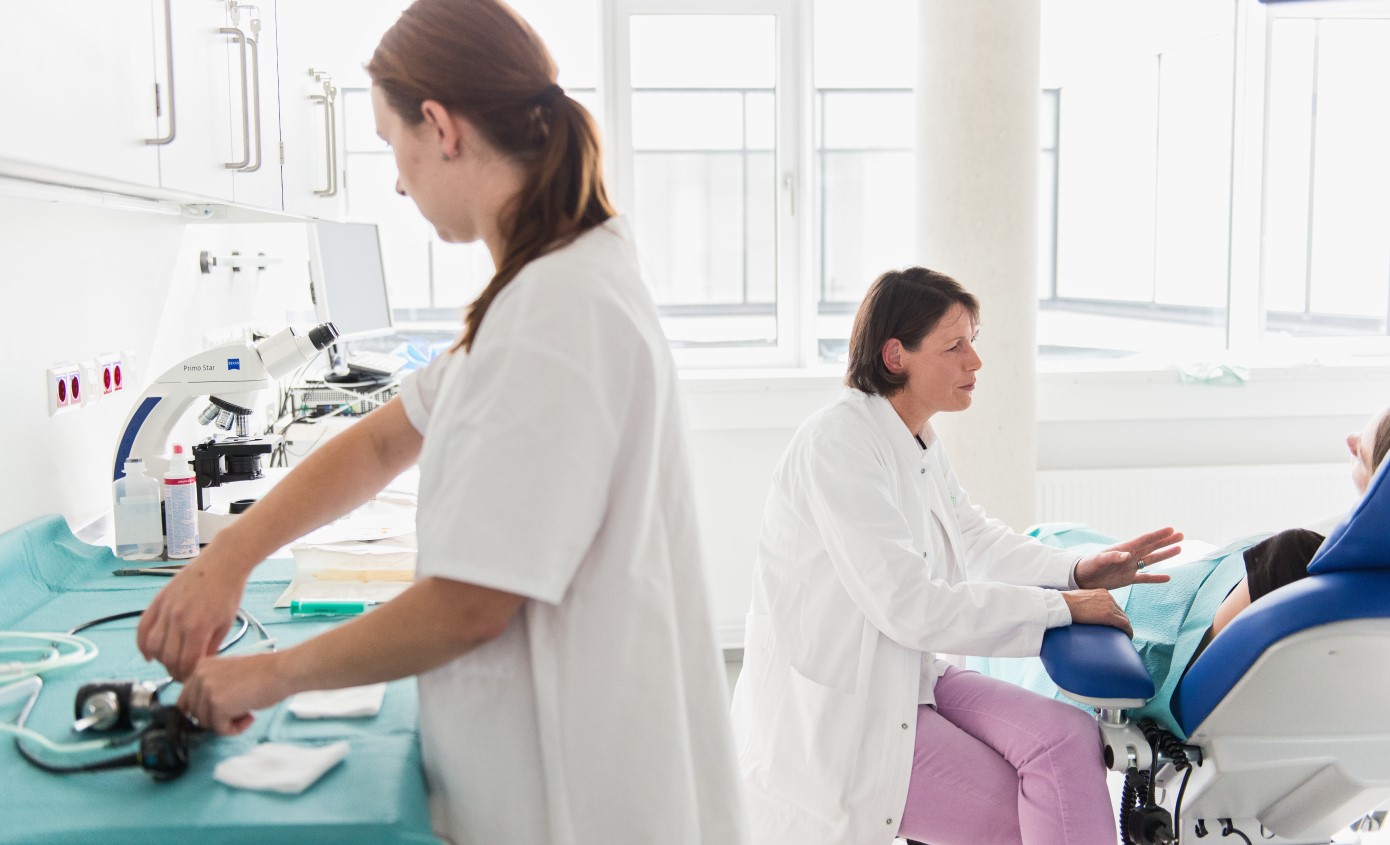 Ärztin berät Patientin, im Vordergrund hantiert eine Arzthelferin.